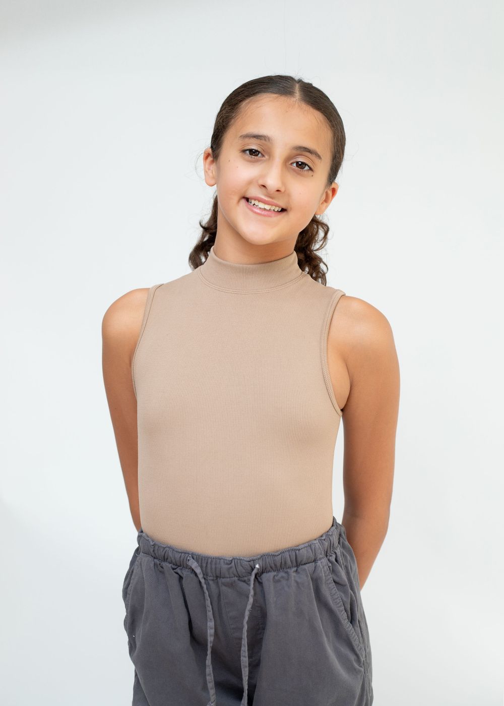Dancer in beige sleeveless top and gray pants poses confidently against white background.