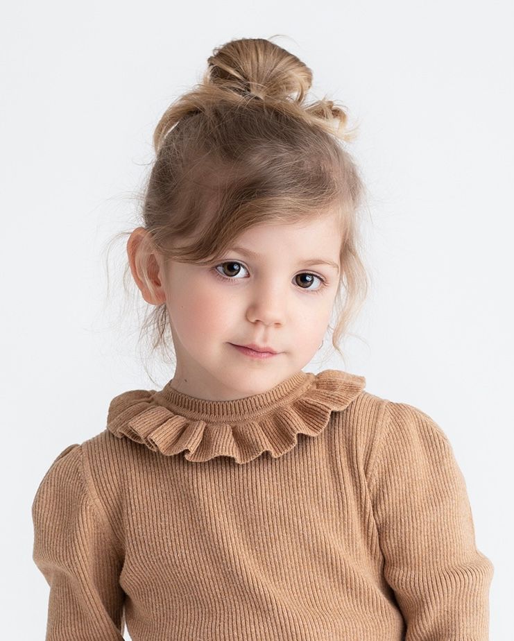 A young subject in a brown ribbed sweater with ruffle collar poses for a portrait.