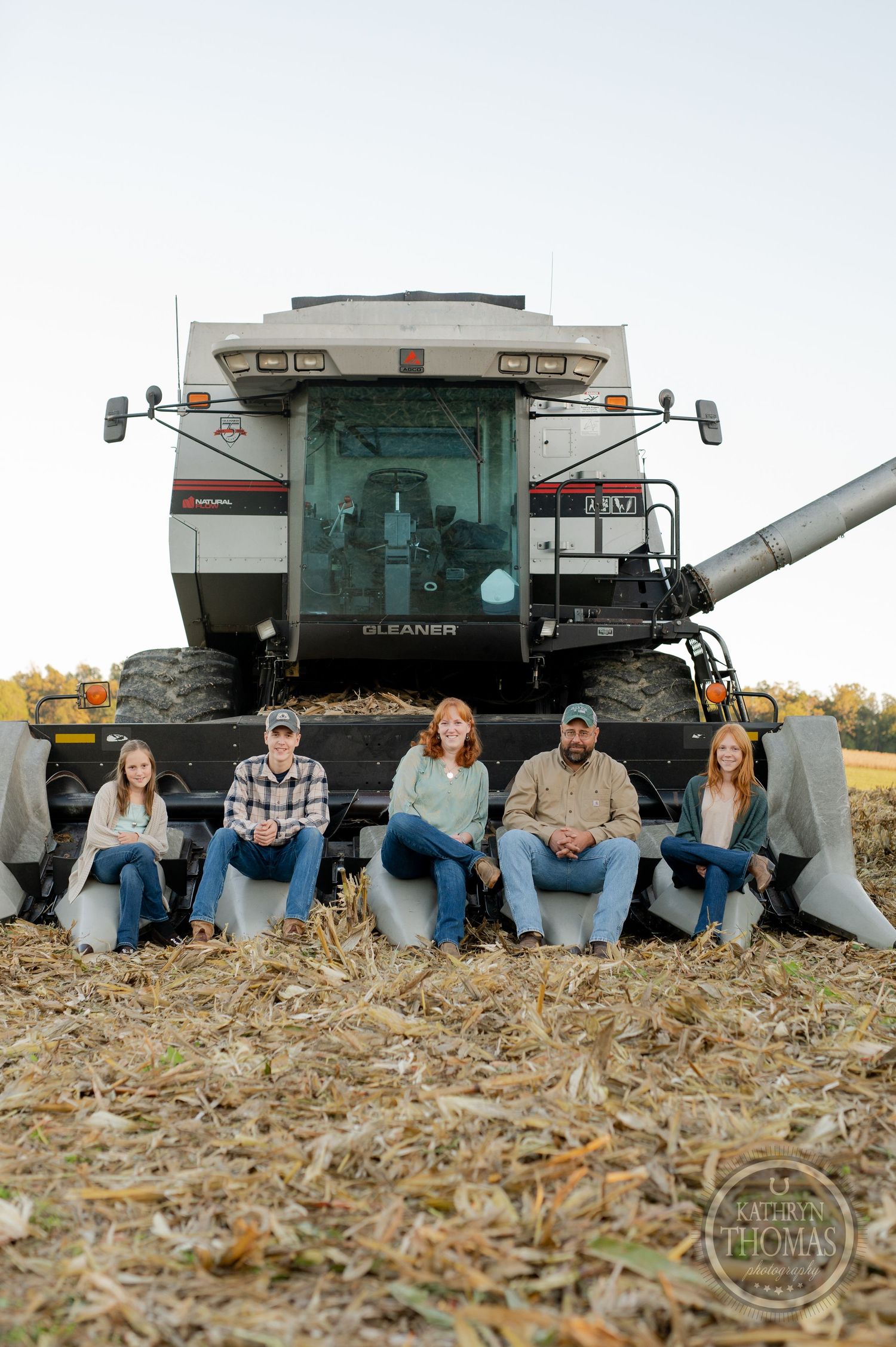 Family members pose seated in front of their modern combine harvester during harvest season.
