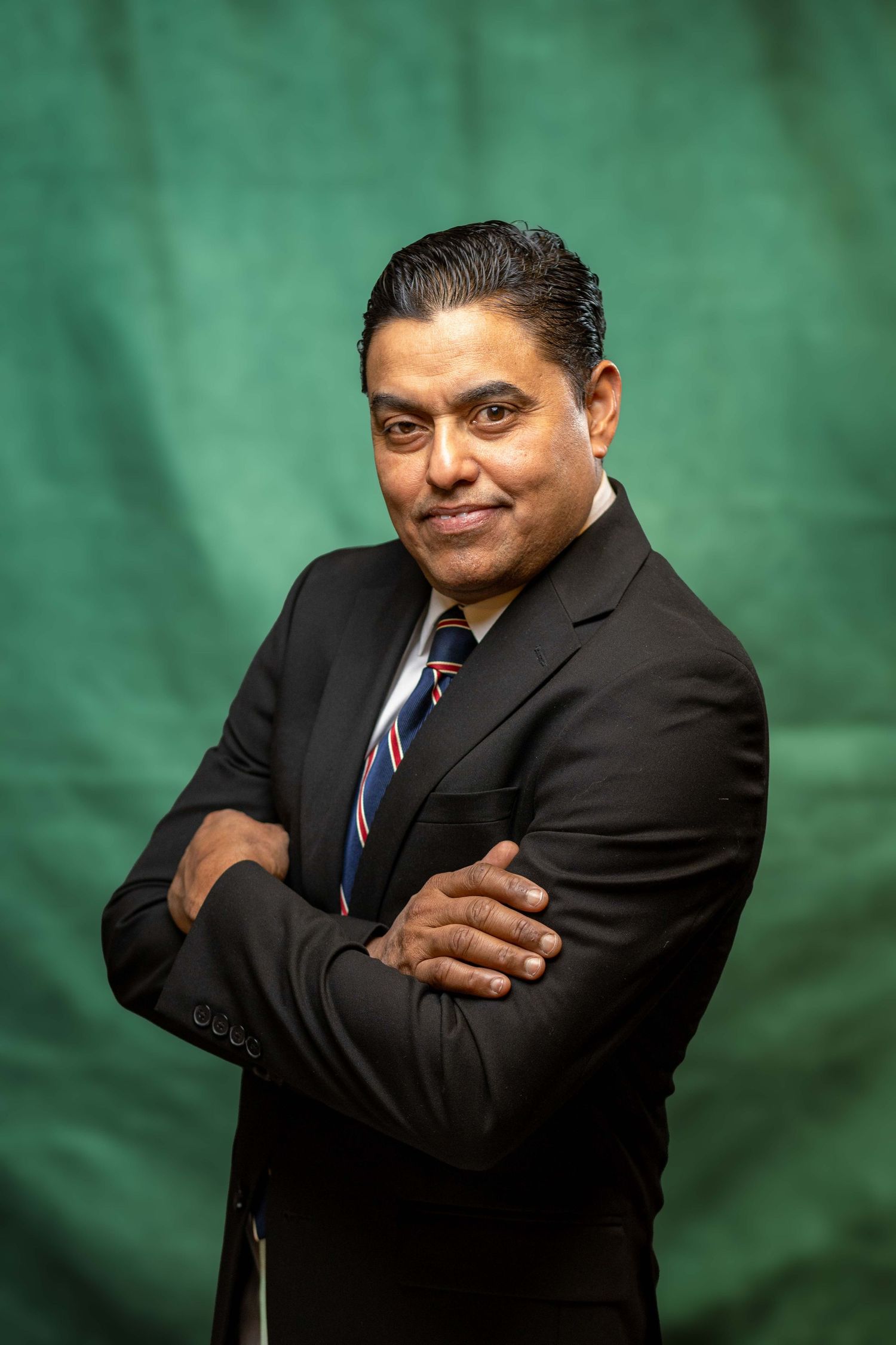 Professional studio portrait of businessman in dark suit against green backdrop.