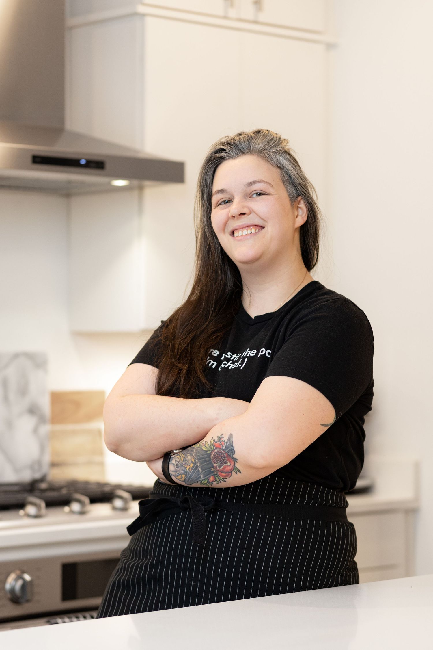 Chef in black uniform smiling while posing in a contemporary kitchen setting.