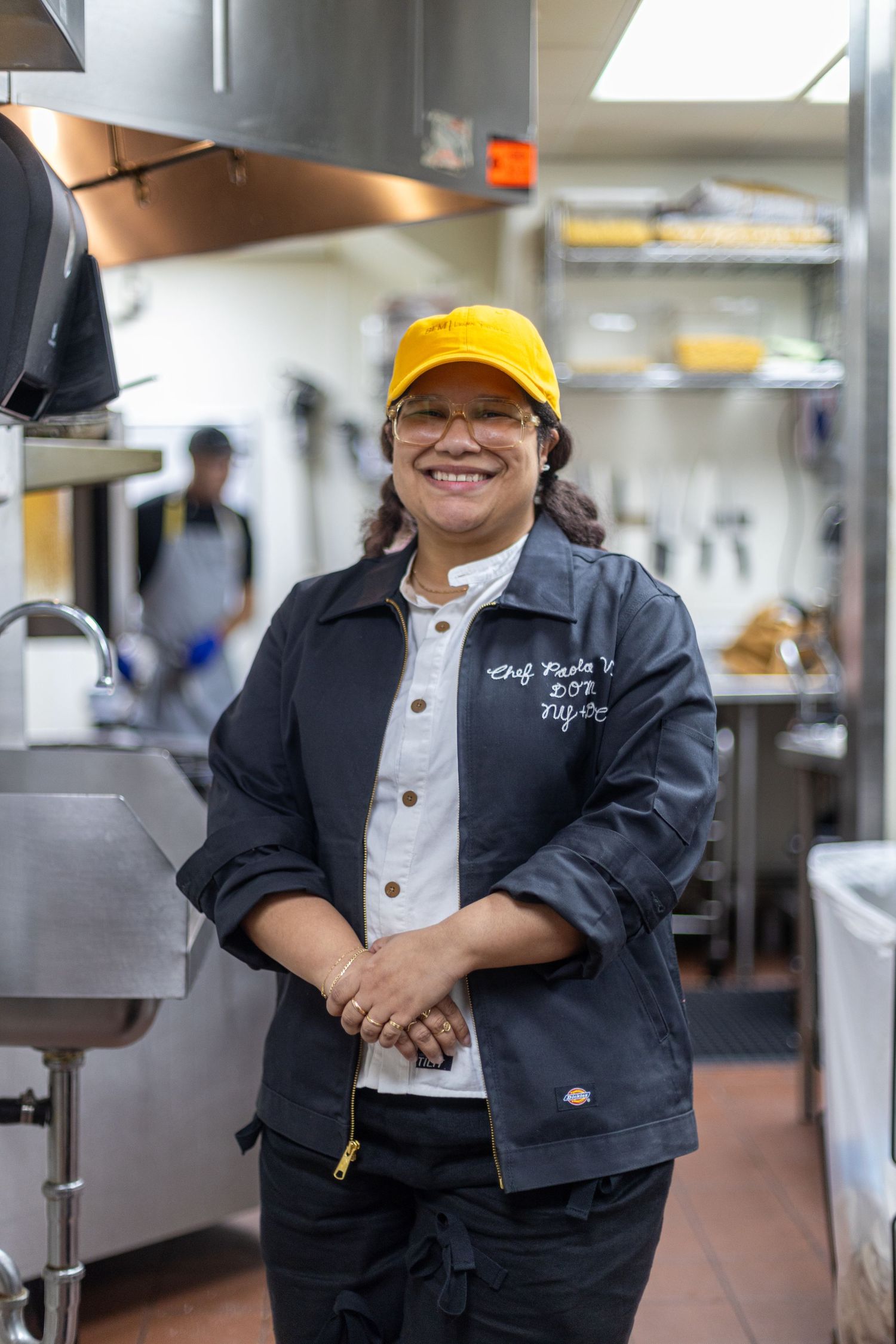 Restaurant worker in yellow cap and work uniform smiling in commercial kitchen.