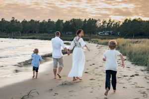 Family walking barefoot along beach shore during golden hour.