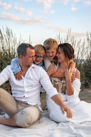 A family sitting together on a white blanket near beach grass at sunset.