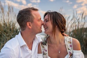 A romantic moment between a couple in white attire against a sunset beach backdrop.
