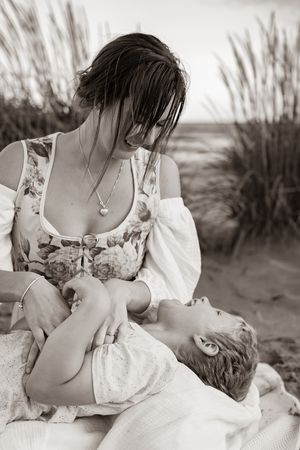 A tender moment between parent and baby among beach grass at sunset, captured in black and white.