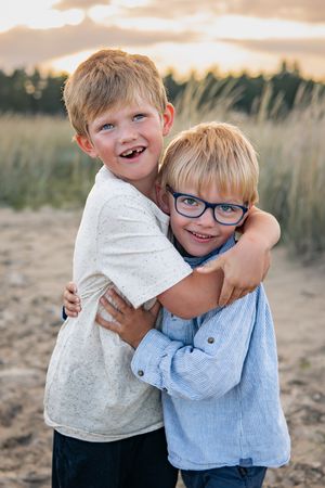 Two young brothers share a loving embrace while smiling outdoors at sunset.