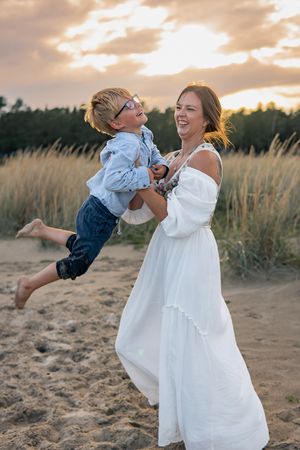 Playful scene of mother and child laughing together on a beach at sunset.