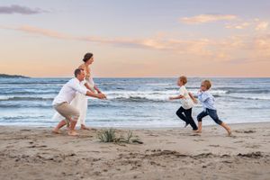 Family playing chase games on the beach at sunset with ocean waves in background.
