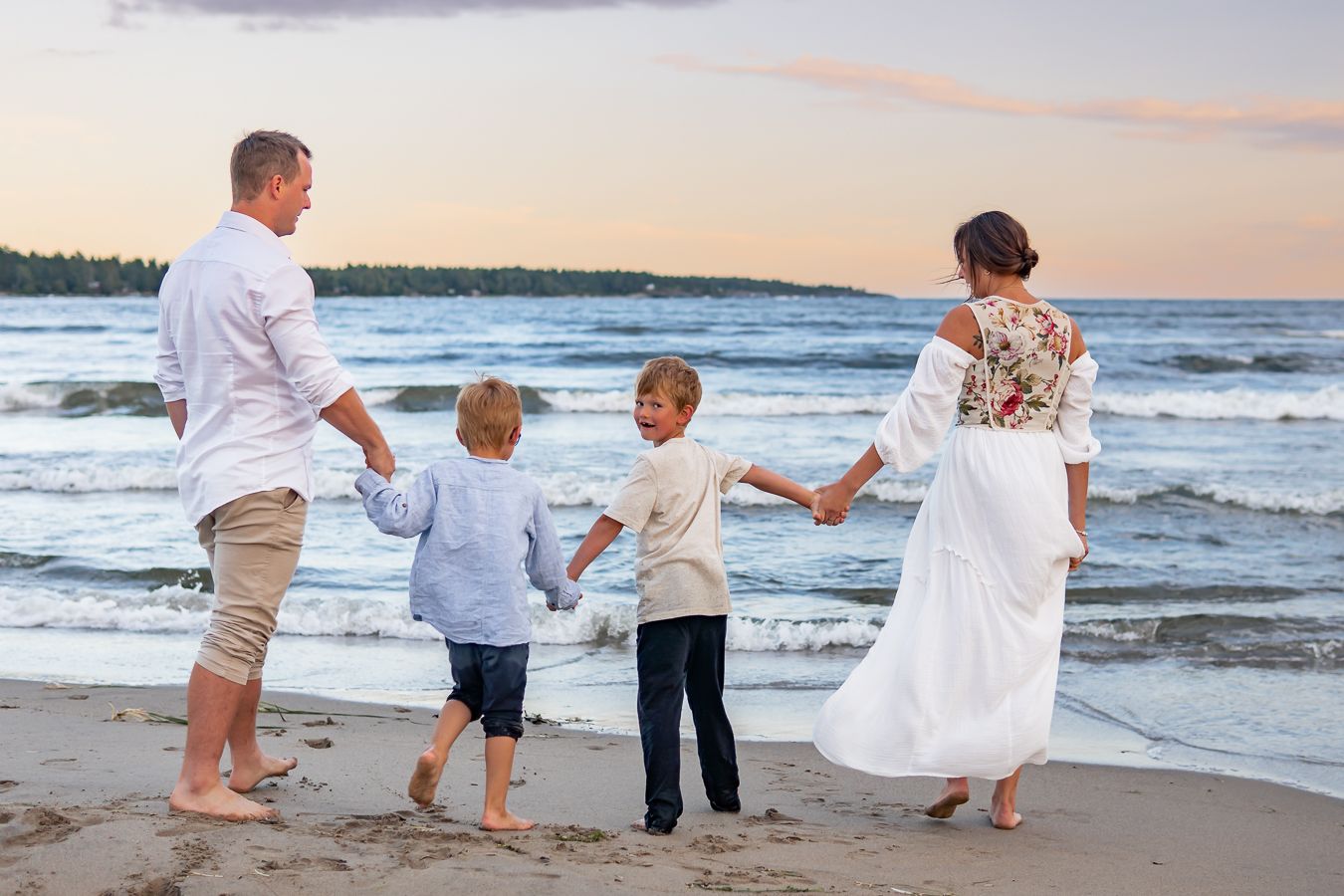 Family holding hands while walking along ocean shore during golden hour.