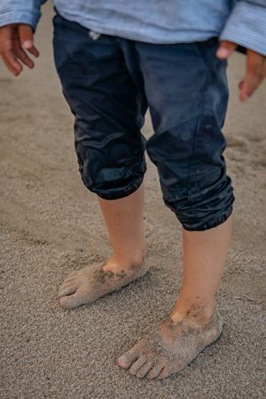 Sandy bare feet on a beach with rolled up jeans.