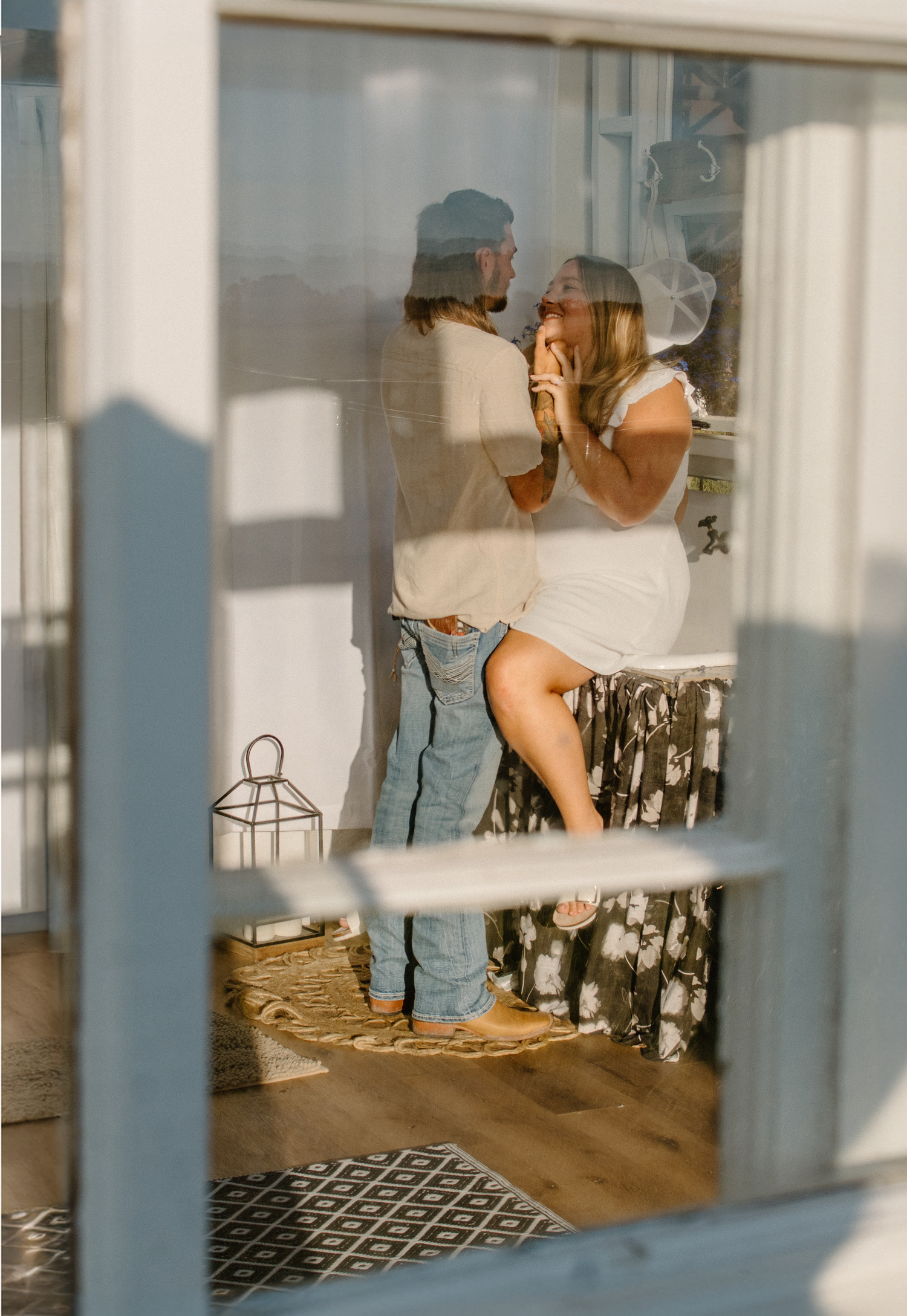 Couple sharing an intimate moment viewed through a window with natural light and shadows.
