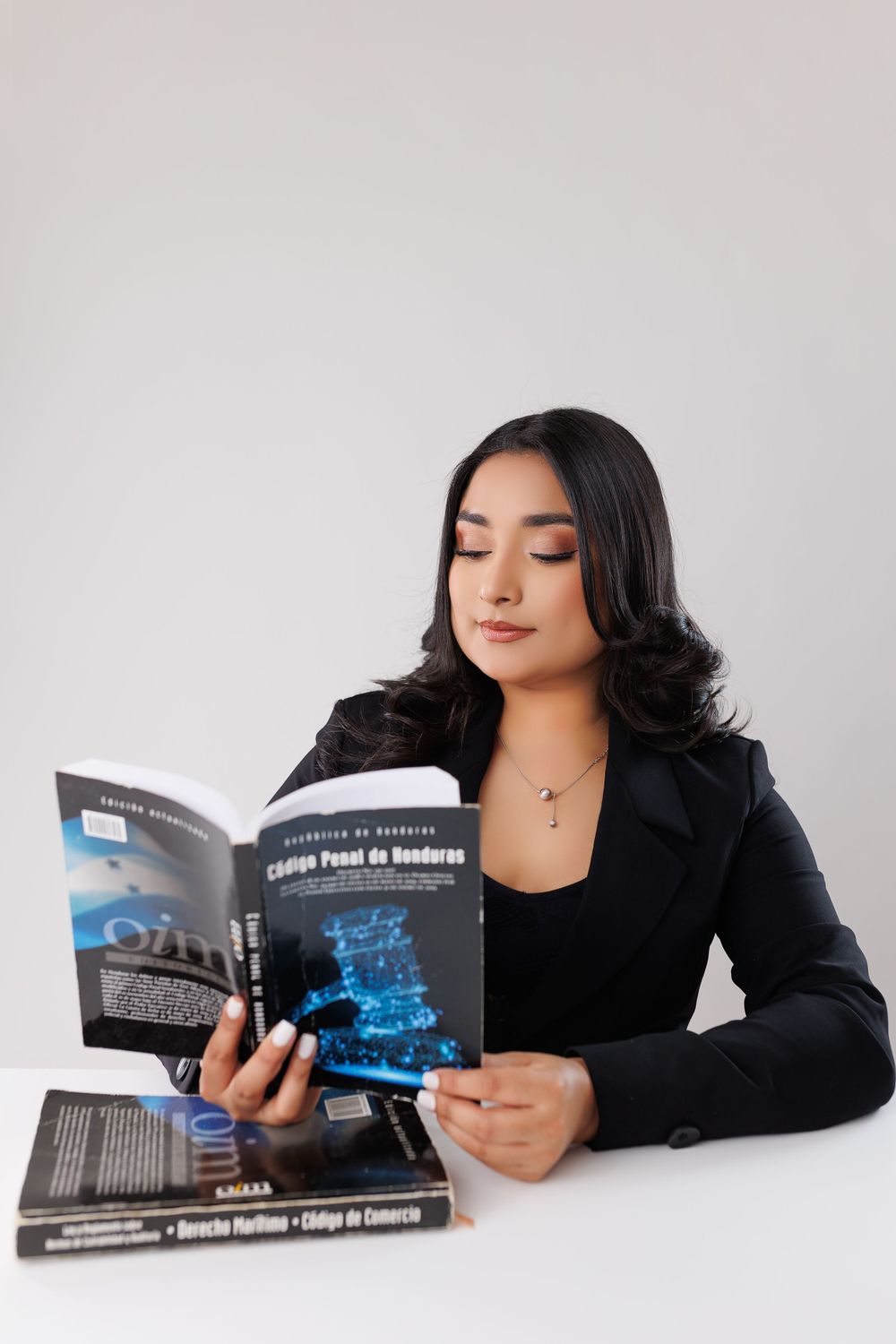 Person in black blazer reading book while lying down during professional photoshoot.