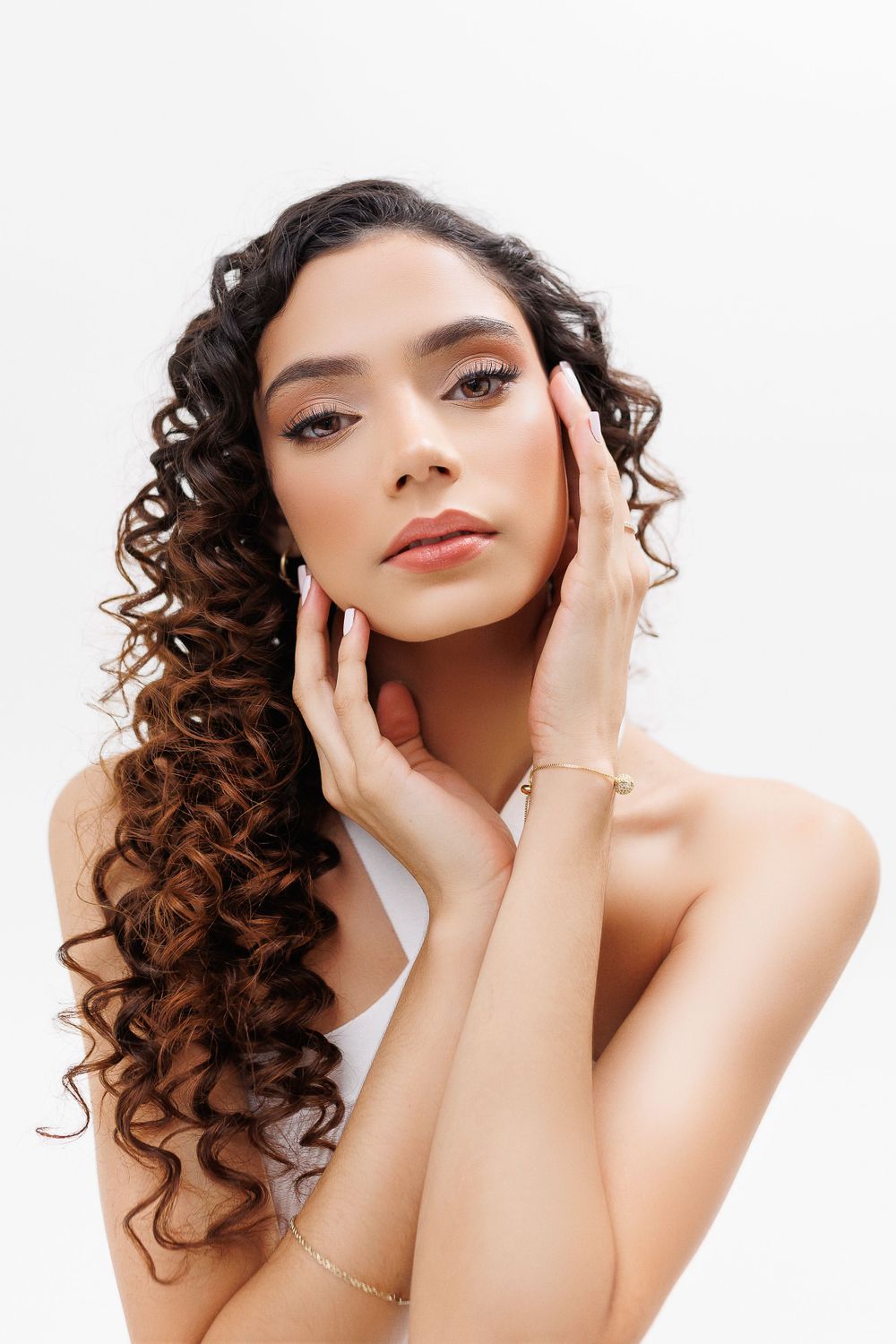 Close-up beauty portrait with curly brown hair and glamorous makeup against white background.