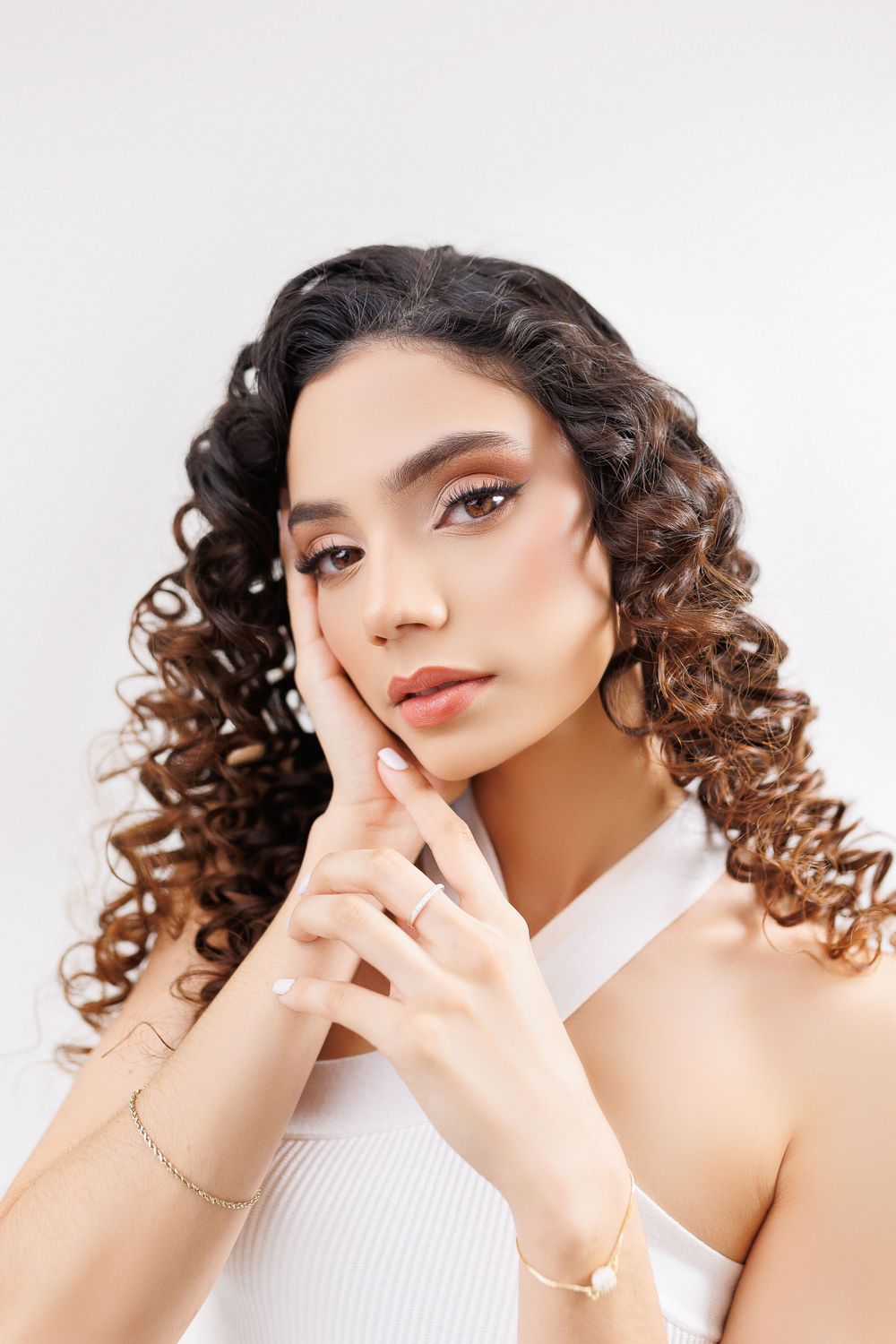 Beauty portrait with curly hair posing with hands near face against white backdrop.