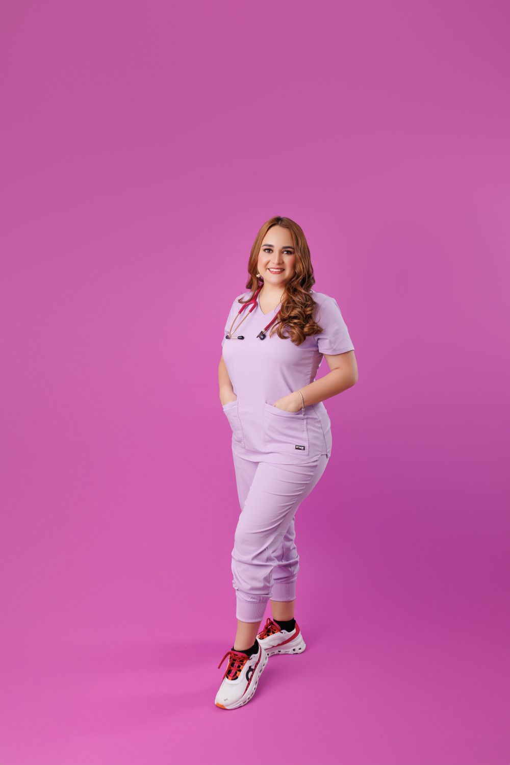 Model in all-white outfit posing playfully against pink background.