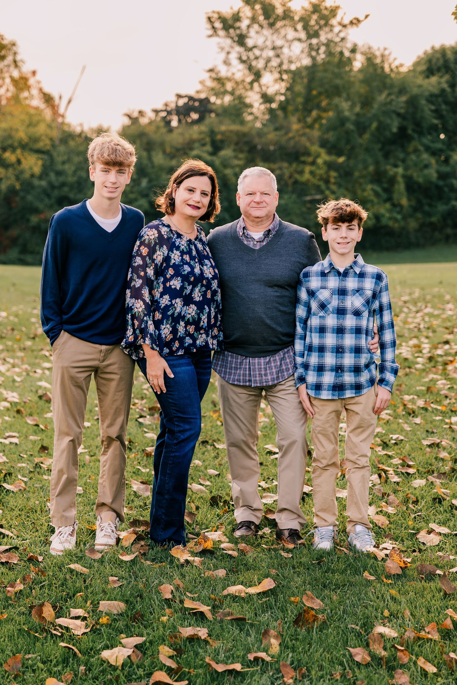 Group of four poses outdoors on autumn grass with fallen leaves, family portrait by Rachel Martinez Photography.
