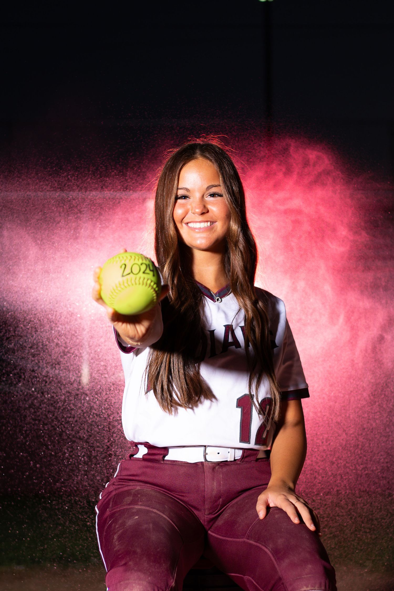 Softball player poses with yellow ball against pink powder background effect.