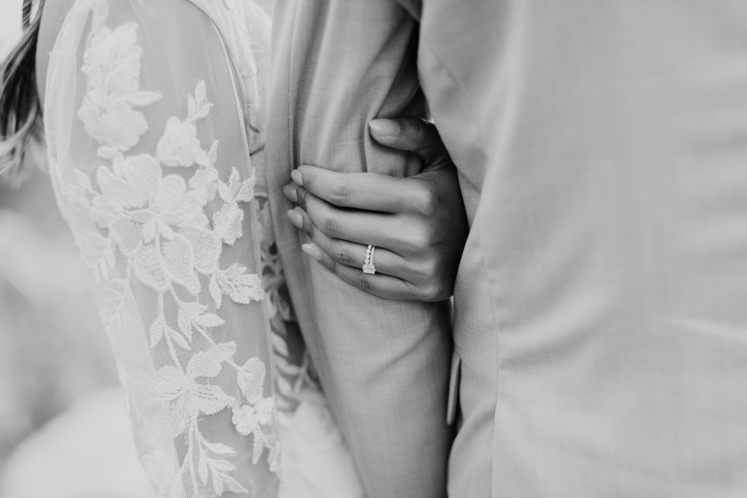 Close-up black and white detail of lace wedding dress and ring.