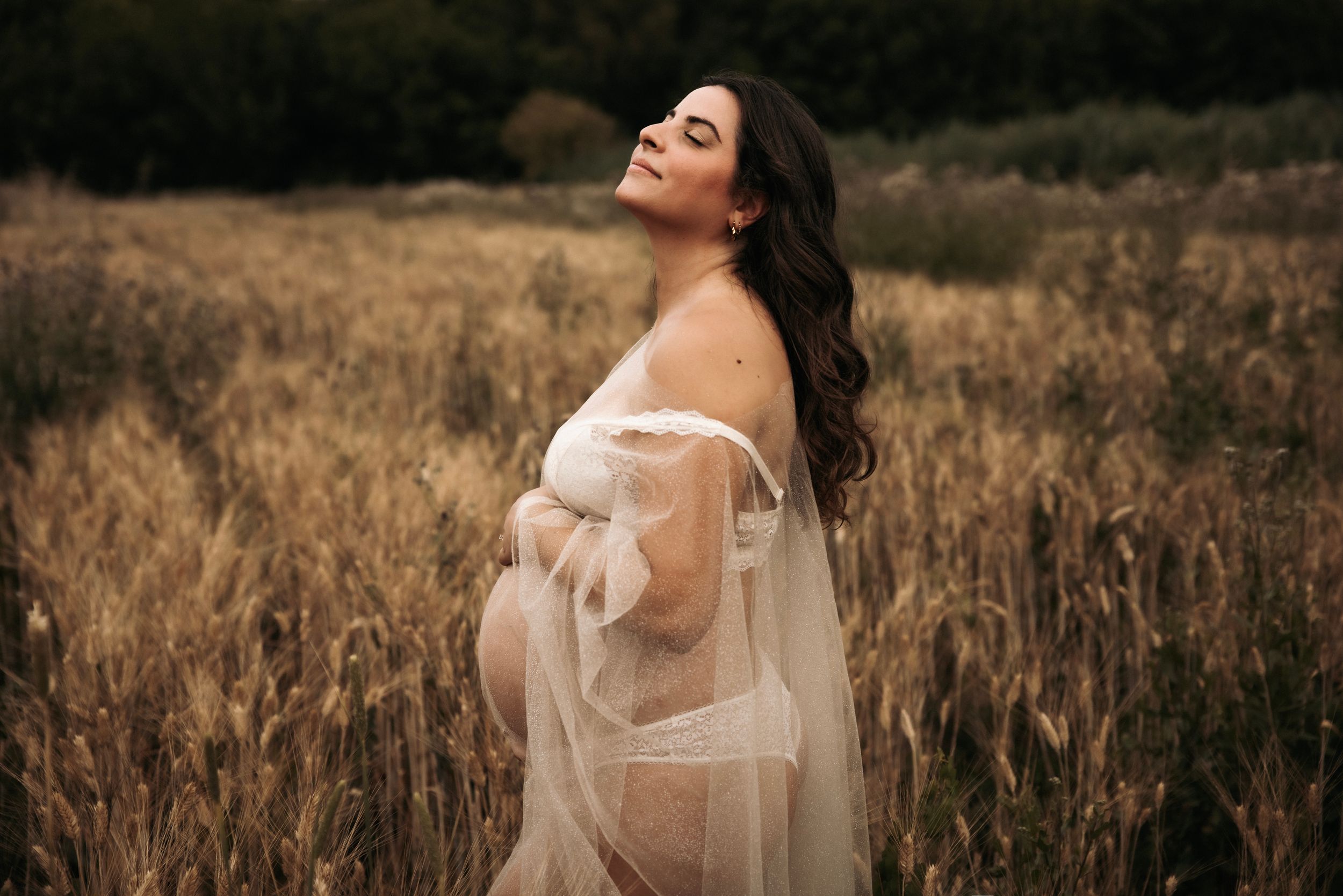 Woman in ethereal white dress poses gracefully in a golden autumn field during sunset.