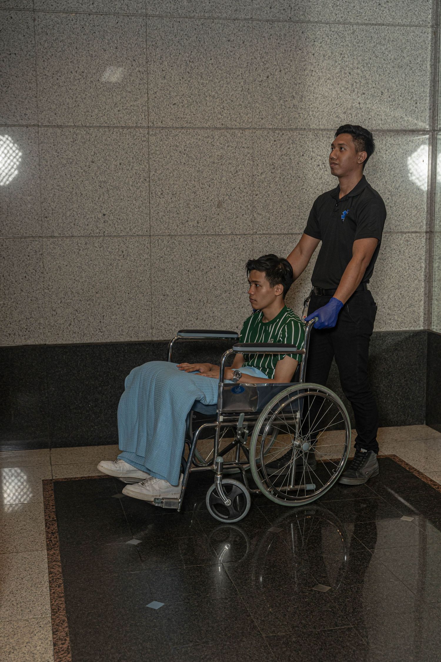 Healthcare worker pushing patient in wheelchair through hospital hallway.