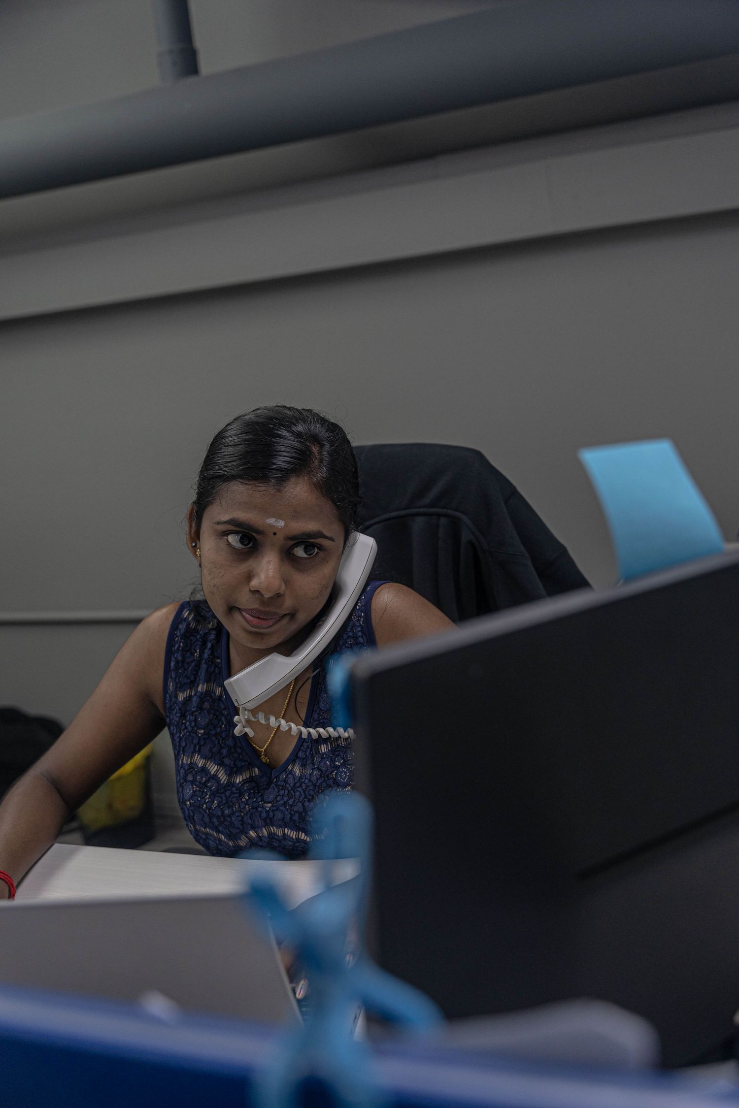 Emergency dispatcher using telephone while working at computer desk in call center.