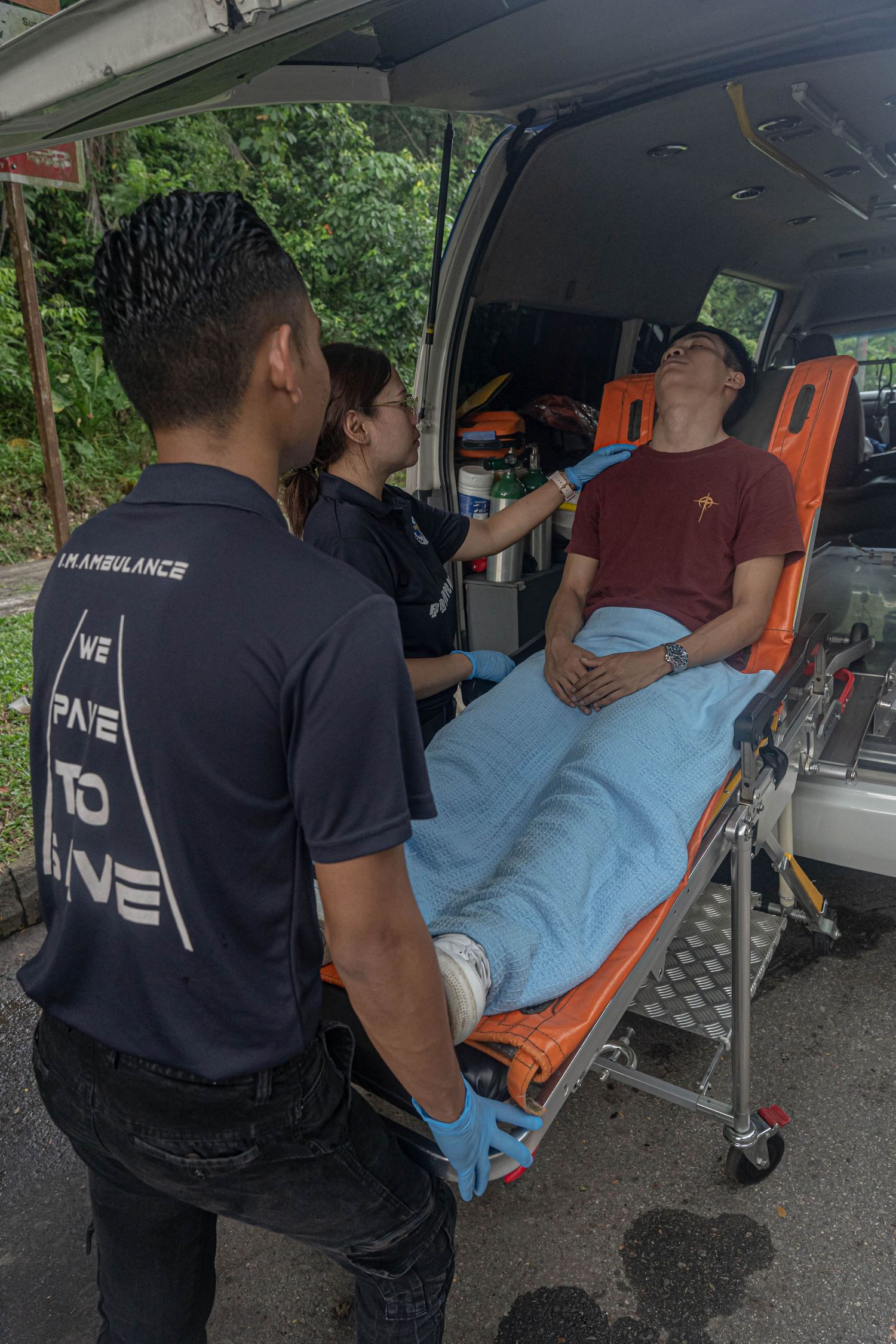 Paramedics loading and securing patient on stretcher into ambulance.