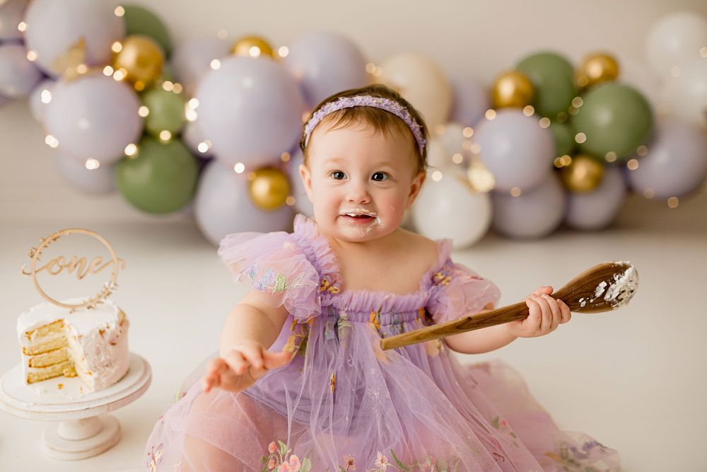 Baby girl in purple tulle dress enjoying cake smash session with balloon backdrop at Summerville SC studio