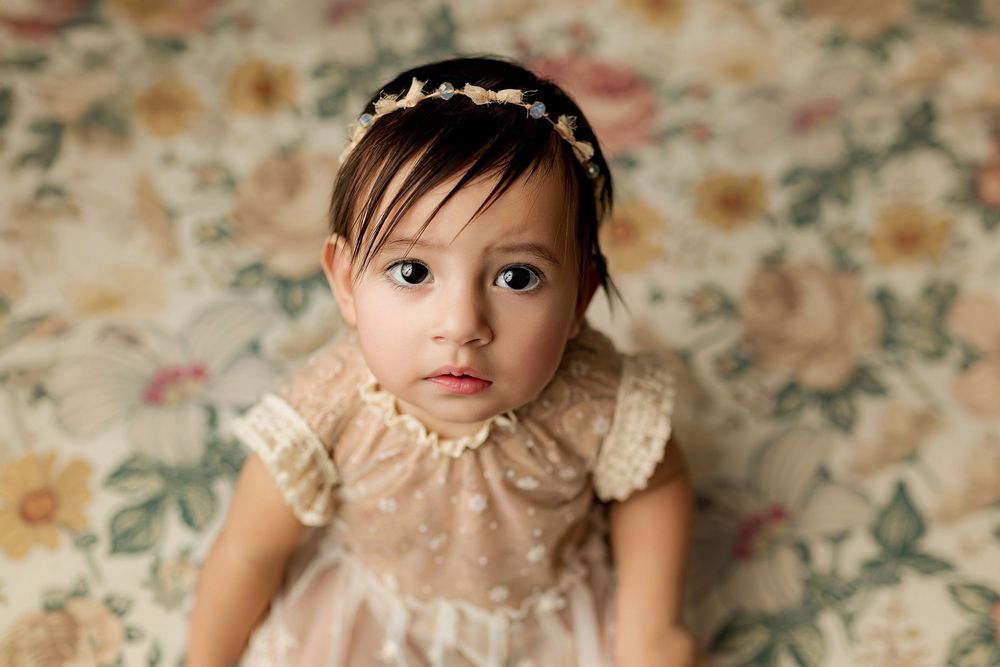 Beautiful baby girl in vintage cream lace dress with floral headband on soft floral backdrop in Summerville SC