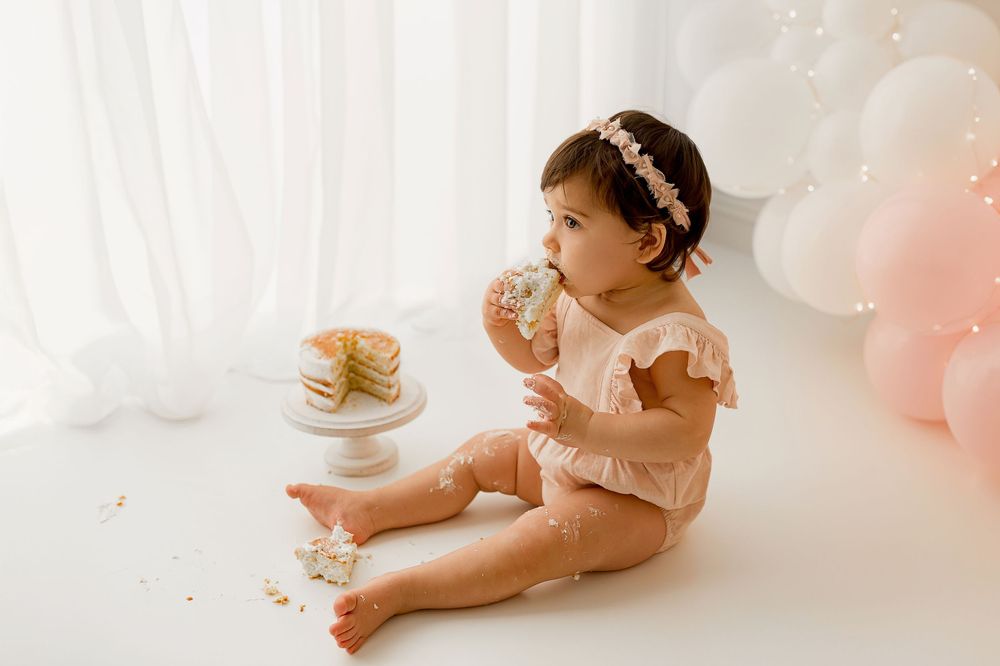 One year old baby girl in pink dress enjoying cake smash session with floral headband at Summerville SC studio