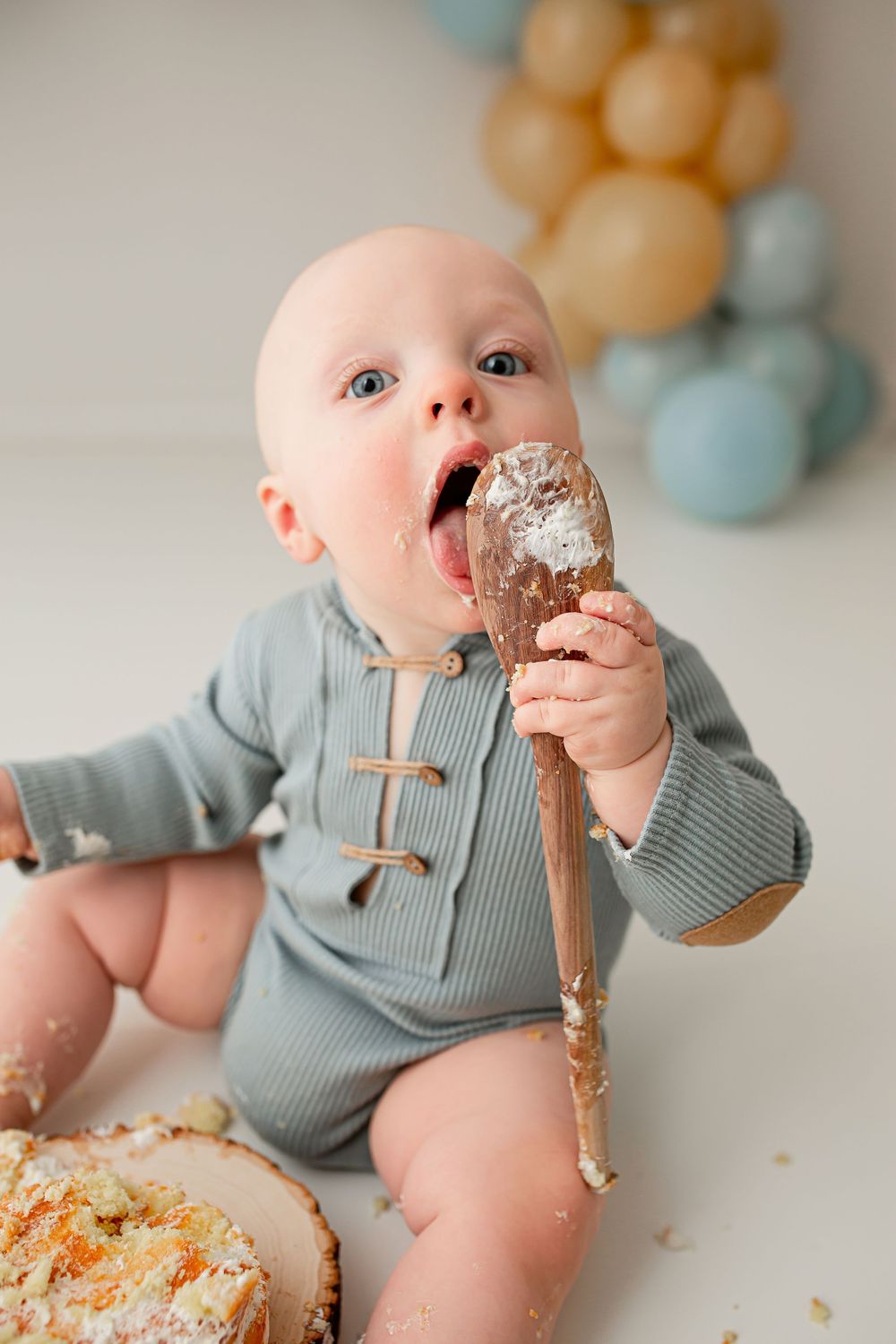 Baby enjoying cake smash session with wooden spoon wearing sage green outfit at Summerville SC photography studio