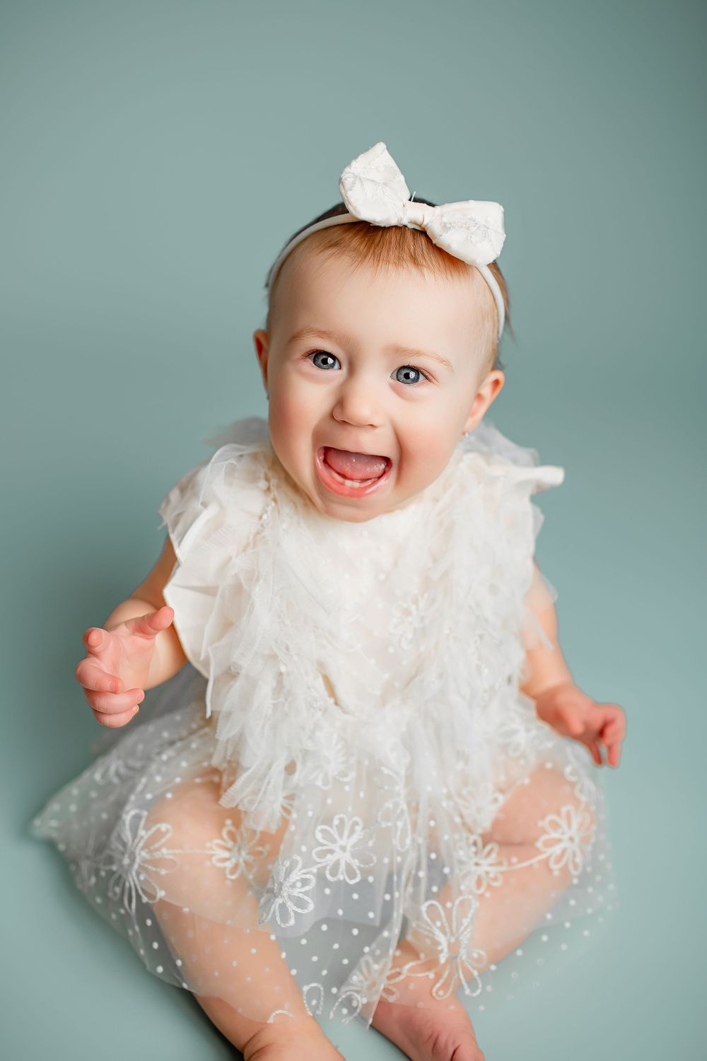 Happy baby girl in white tulle dress and bow headband during milestone portrait session in Summerville SC studio