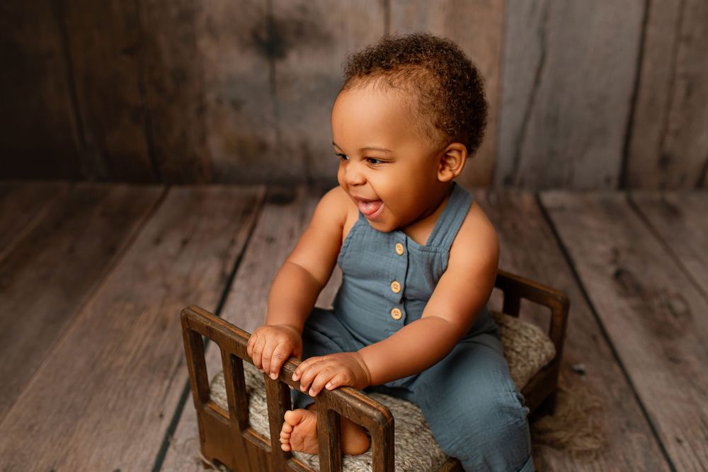 Happy milestone baby in blue romper sitting on wooden chair during studio portrait session in Summerville SC