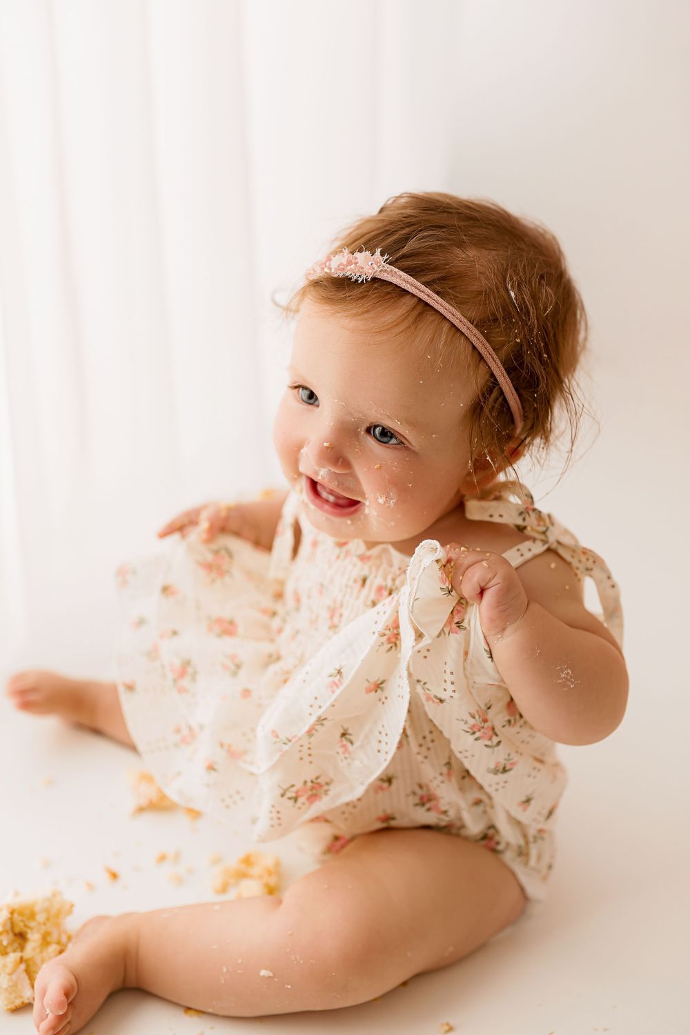 Adorable one year old baby girl in floral dress with pink headband during cake smash session in Summerville SC