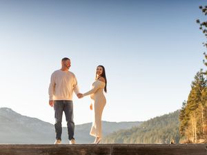 A couple stands together on a mountain overlook during golden hour as sunlight illuminates the scenic landscape.