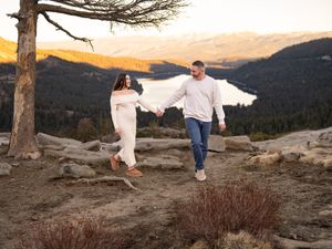 A couple walks along a scenic mountain overlook at sunset with dramatic orange skies and mountain vistas in view.