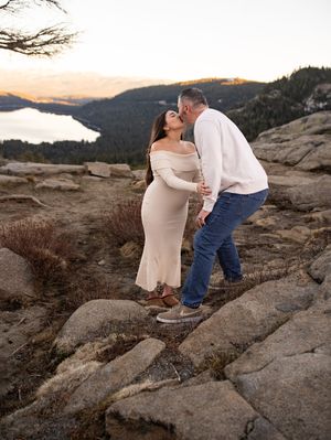 A romantic maternity photo on a mountain overlook with a scenic lake view at sunset.