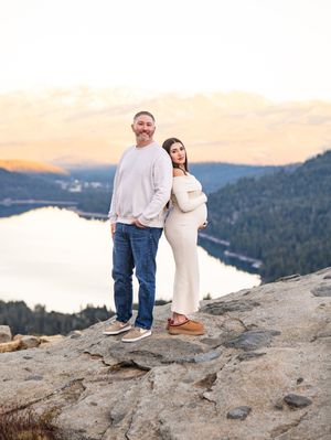 A couple poses on rocky mountain terrain overlooking a serene lake during golden hour.
