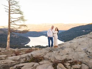 A scenic mountaintop maternity photo with a lake vista and bare tree in the background.