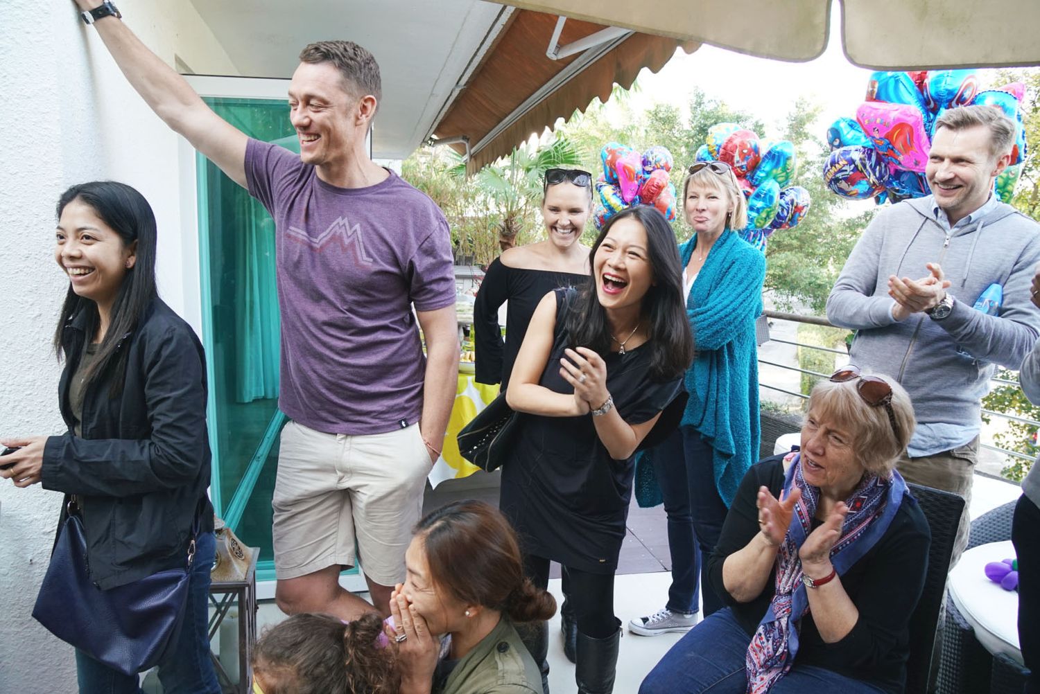 A group gathers around a decorated birthday cake at a celebration party with colorful decorations in the background.一群人圍坐在裝飾精美的生日蛋糕旁，背景是色彩繽紛