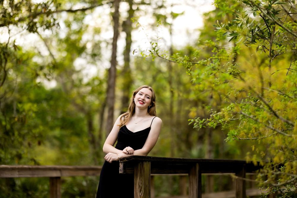 A person in a black dress poses gracefully in a lush green outdoor setting during golden hour.