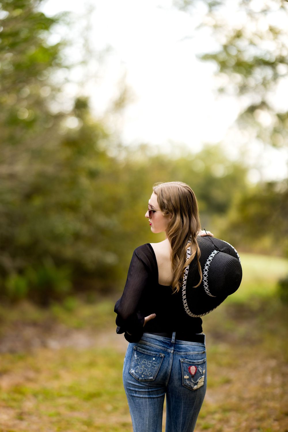 Person wearing a black hoodie and blue jeans stands in a natural outdoor setting with blurred background.