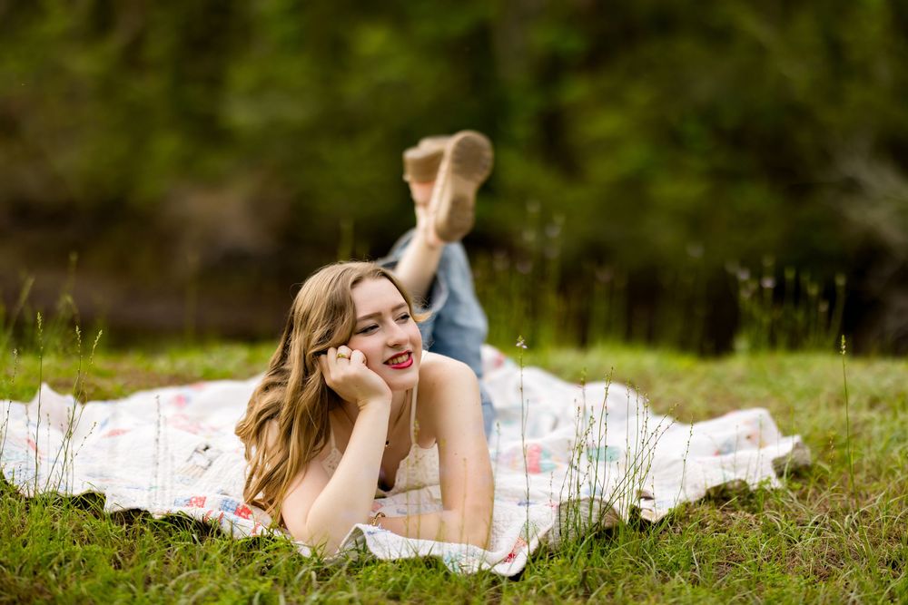 Person lying on white blanket in grassy field during outdoor summer photoshoot.