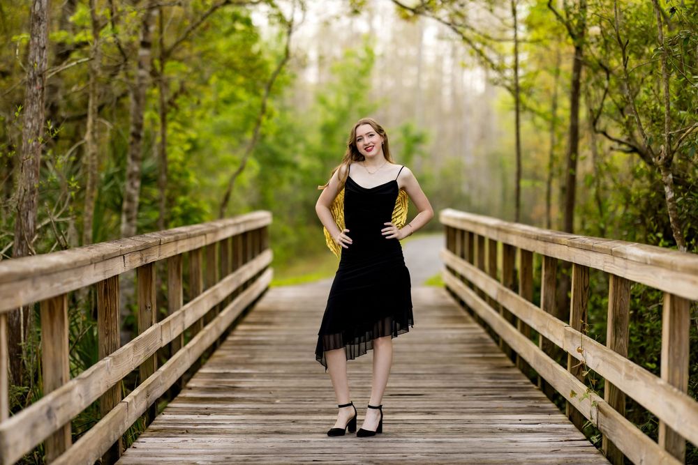 A wooden boardwalk path through a lush green forest with a person in black standing at the end.
