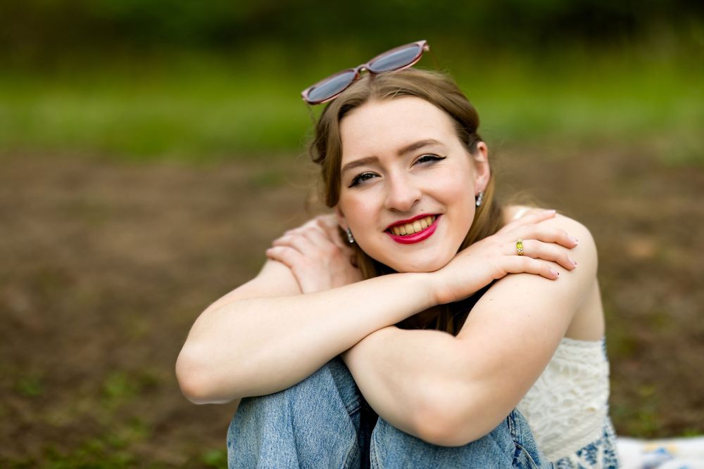 A person wearing a blue denim jacket sits outdoors in a natural setting with a blurred green background.
