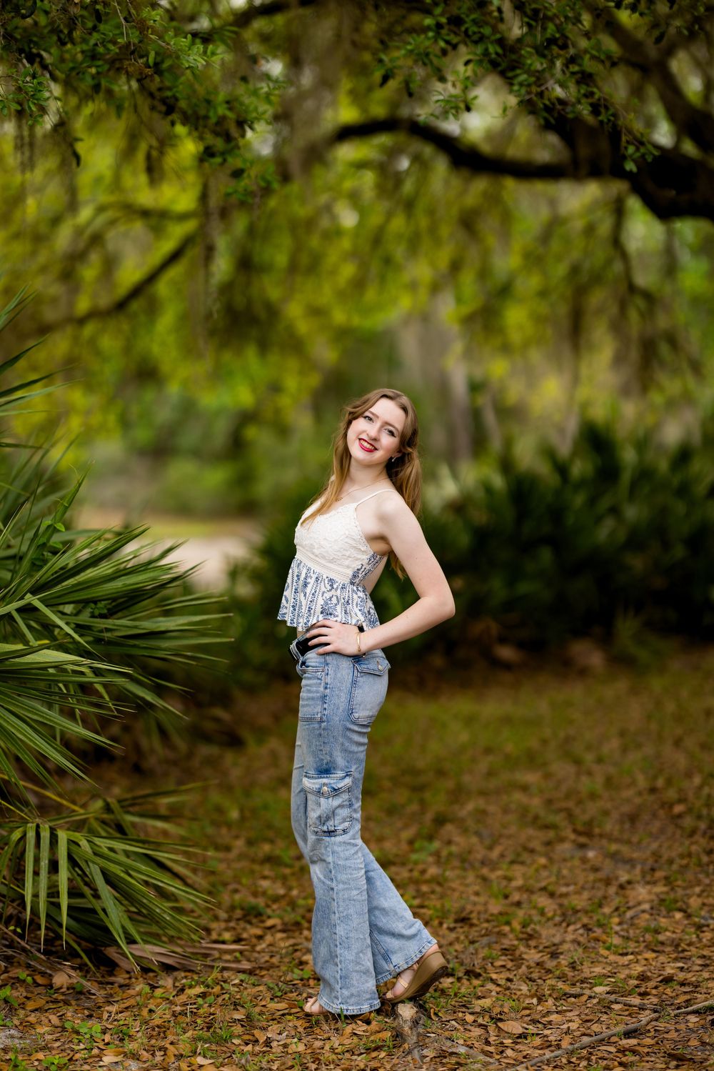 A casual outdoor portrait in a lush garden setting with Spanish moss and palm fronds framing the natural scene.