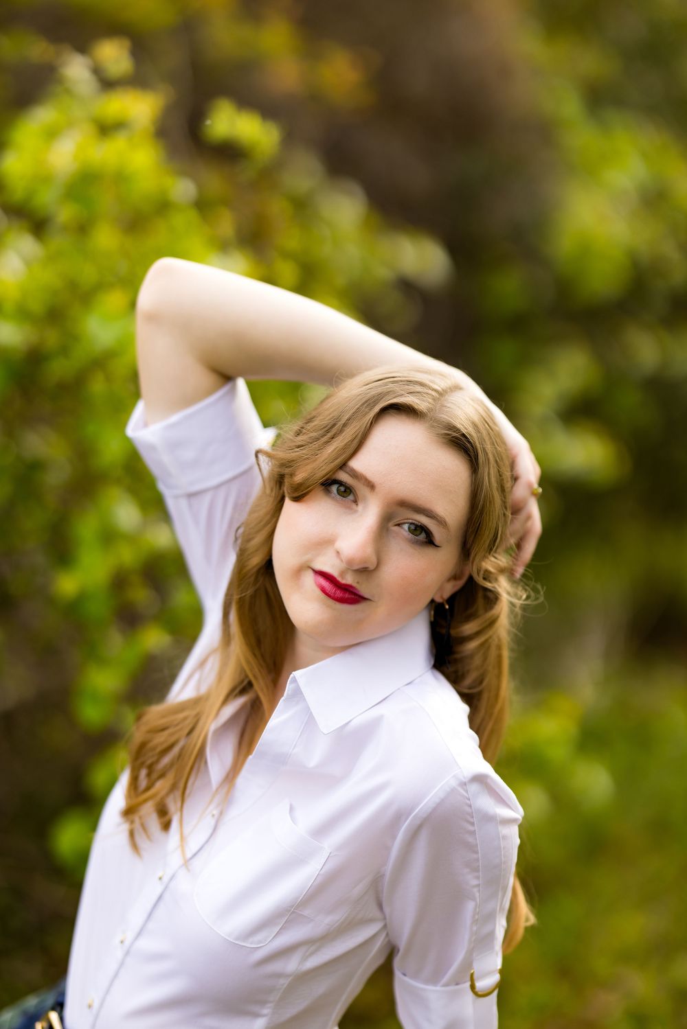 A person in a white button-down shirt poses playfully against a blurred green nature background.