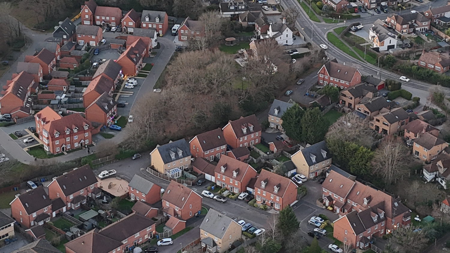 Aerial view of residential neighborhood with orange-roofed houses and winding streets in a suburban setting.