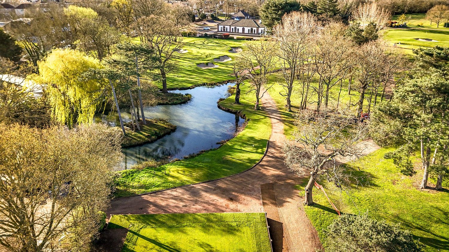 Scenic aerial view of a winding river through a lush green golf course with trees and pathways on a sunny day.