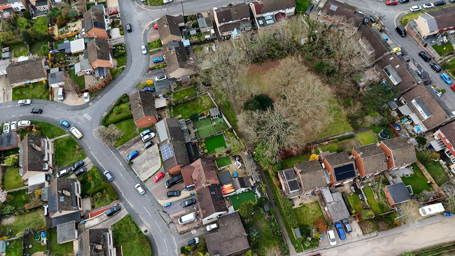 Aerial view of residential suburban neighborhood with winding streets and houses surrounded by trees.